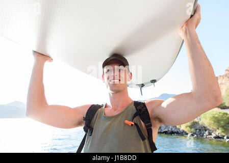 Caucasian man carrying paddleboard at river Banque D'Images