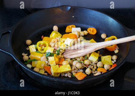 Ci-dessus (top) vue de cuillère en bois en remuant le tofu, Faro et les légumes dans la poêle en fonte - vegan food concept Banque D'Images