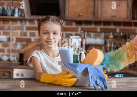 Adorable petite fille avec des produits de nettoyage à la caméra à la maison à Banque D'Images