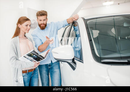 Heureux couple holding catalogue et choisir en voiture salon concessionnaire Banque D'Images