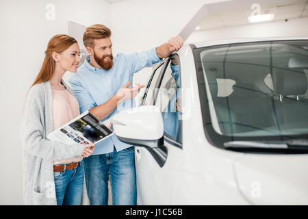 Heureux couple holding catalogue et choisir en voiture salon concessionnaire Banque D'Images