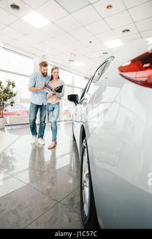 Heureux couple holding catalogue et choisir en voiture salon concessionnaire Banque D'Images