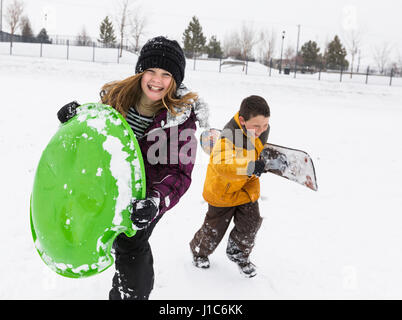 Smiling boy and girl exerçant son toboggan et snowboard en hiver Banque D'Images