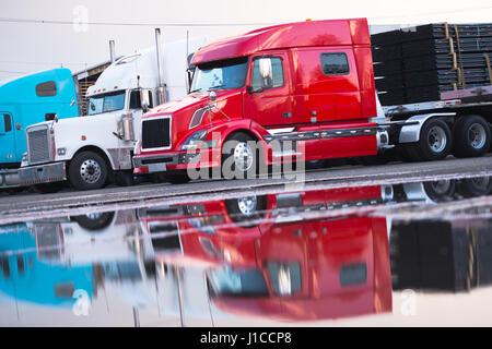 Plusieurs gros camion camions semi de différents modèles et couleurs de classique et de rouge et blanc avec une remorque sur le parking avec une charge Banque D'Images