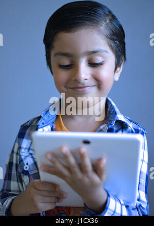 Kid with tablet computer. La pensée de l'enfant holding tablet. Smiling kid avec la technologie numérique à la recherche à la tablette. Banque D'Images