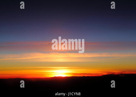 Vol d'un avion dans le ciel avec traînée au coucher du soleil Banque D'Images