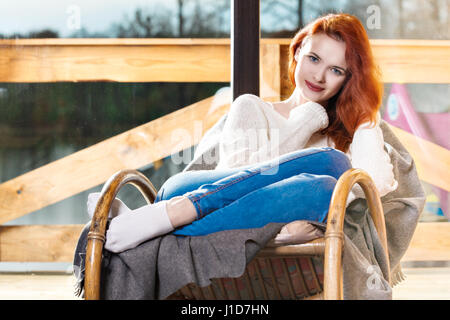 Attrative red-haired woman resting assis sur un fauteuil à bascule en face de la fenêtre. Calme et confort. Banque D'Images