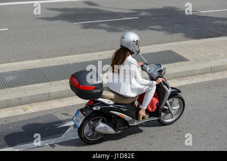 Jeune femme en tailleur-pantalon blanc est le moteur de scooter dans la rue de Barcelone, Catalogne, Espagne. Banque D'Images