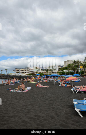 La plage de touristes sur le sable volcanique noir en jour nuageux à Puerto de Santiago, Tenerife, Canaries, Espagne. Banque D'Images