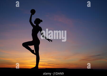 Danseuse dans la dance ne le divise dans l'air contre le coucher du soleil Banque D'Images