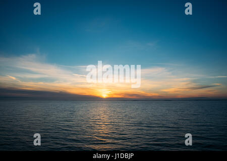 Magnifique coucher de soleil sur la mer Baltique, la lumière du soleil reflétant sur l'eau, nuages d'or et ciel bleu profond Banque D'Images