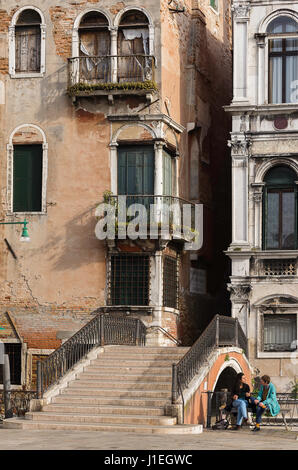 Deux dames assis sur un côté du canal parle banc à côté d'un pont, Venise, Italie Banque D'Images