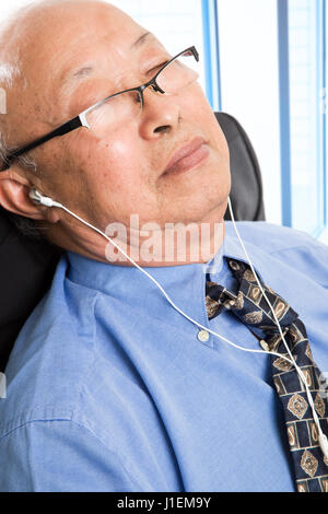 La prise d'un senior asian businessman relaxing et écouter de la musique dans le bureau Banque D'Images