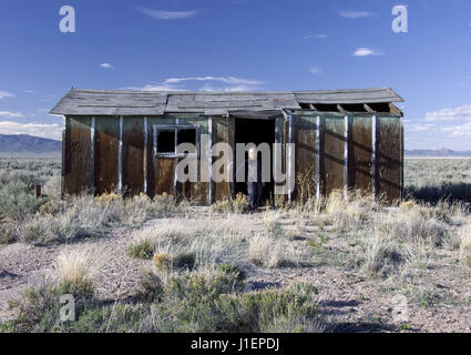 Un jeune garçon vêtu de combinaisons noires se tient à l'entrée d'une maison abandonnée dans une vallée éloignée dans l'Utah rural. Banque D'Images