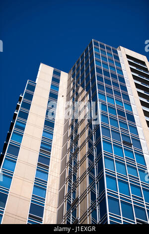 Détail d'une tour moderne en construction à plusieurs niveaux avec des angles droits, avec des fenêtres en verre bleu foncé avec des armatures en métal et les murs en pierre recouverts de Banque D'Images