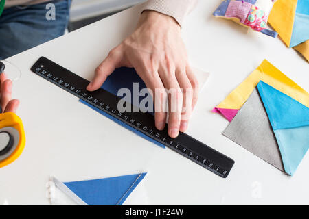 Patchwork et broderie à l'atelier - gros plan sur les mains de l'homme, qui mesure une gamme de patchs colorés de tissu sur le bureau pour coudre la toile. Banque D'Images