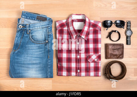 Tenues décontractées pour hommes avec des accessoires sur une table en bois, chemise à carreaux rouge et bleu jeans avec des lunettes, bracelet, porte-monnaie, ceinture brune et regarder, top vie Banque D'Images