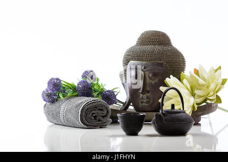 Tête de Bouddha au-dessus du socle sur un fond blanc, serviette, verre, fleur de lotus et d'une réflexion Banque D'Images