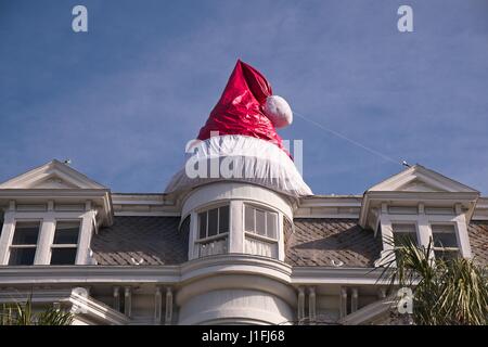 Un géant Santa hat tops le toit d'une maison historique décorée pour Noël sur Meeting Street à Charleston, SC. Banque D'Images