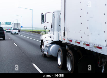 Semi-classique blanc professionnel camion avec remorque blanc pour transporter du fret industriel transporte un chargement sur la route avec les autres usagers de la route par temps de brouillard Banque D'Images