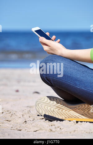Close up of a woman using smartphone sur une plage, vue de côté. Banque D'Images