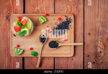 Thé noir avec des cuillères en bois sur une planche en bois décoré de feuilles de menthe, kiwi, banane, morceaux de pamplemousse et citron vert, les baies du сranberrie Banque D'Images