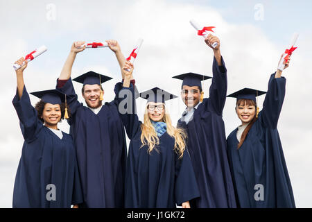 Heureux les étudiants dans les conseils de mortier en agitant des diplômes Banque D'Images