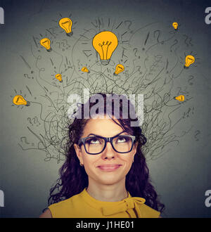 Jeune femme à lunettes avec beaucoup d'idées au-dessus de la tête des ampoules à haut isolé sur fond de mur gris. La créativité d'Eureka concept Banque D'Images