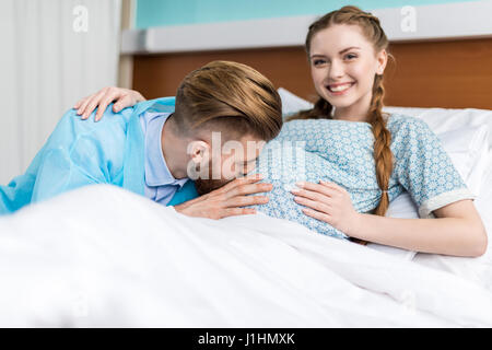 Smiling pregnant woman with husband kissing ventre à l'hôpital Banque D'Images