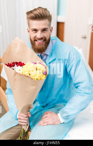 Vue avant de l'heureux jeune homme avec des fleurs à l'hôpital Banque D'Images