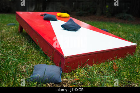 Conseil cornhole rouge et blanc toss jeu avec poufs sur l'herbe dans le jardin Banque D'Images