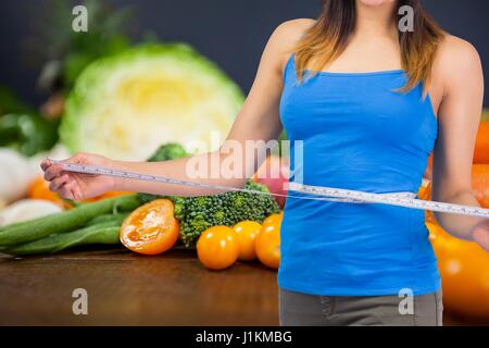 Digital composite de Midsection of woman measuring waist avec légumes en arrière-plan Banque D'Images