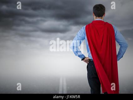 Digital composite de retour de l'homme d'affaires avec les mains sur les hanches du super-héros contre road et ciel orageux Banque D'Images