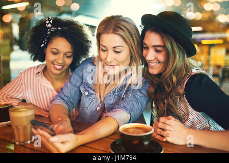 Jeune femme montrant amis quelque chose sur son téléphone portable, assis ensemble autour d'un café détente dans une cafétéria Banque D'Images