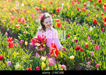 Enfant dans le champ de fleurs de tulipe. Petite fille douce coupe tulipes au jardin d'été ensoleillé. Kid avec bouquet de fleurs pour maman jour ou cadeau d'anniversaire. Todd Banque D'Images