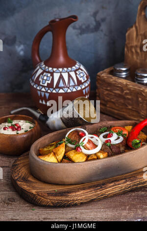 Viande grillée avec des pommes de terre, ojaxuri géorgien traditionnel, lave avec du vin rouge sur une table en bois. Banque D'Images