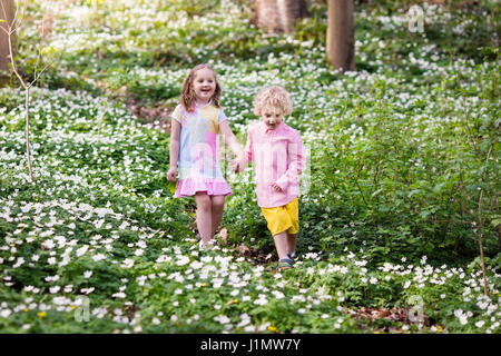 Cute little girl and boy playing dans blooming spring park avec les premières fleurs anémone sauvage blanc. Enfants sur chasse aux œufs de Pâques dans le jardin en fleurs. Les enfants p Banque D'Images