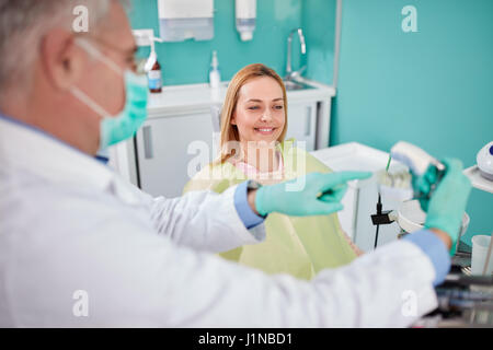 Les jeunes sourire femme en fauteuil dentaire Voir modèle de la mâchoire en mains dentiste Banque D'Images