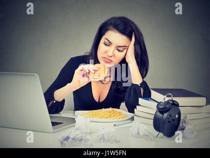 La sédentarité et la malbouffe concept. Fatigué a souligné femme assise à son bureau et hamburger frites Banque D'Images