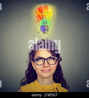 Portrait d'une femme avec des lunettes et idée créative à la recherche jusqu'à l'ampoule colorée sur fond de mur gris. Concept d'inspiration Banque D'Images