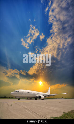 Avion de passagers roulant blanc le long de la voie de circulation après l'atterrissage à l'aéroport sur le coucher du soleil Banque D'Images