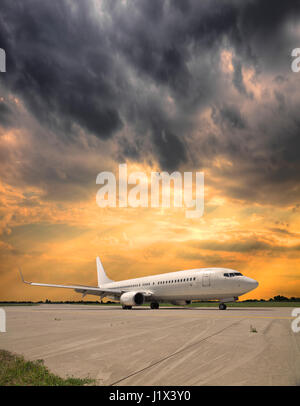 White passenger plane le roulage à l'aéroport après l'atterrissage sur un coucher de soleil d'été orageux Banque D'Images