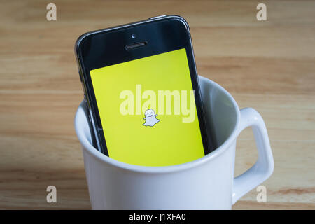 Bangkok, Thaïlande - 22 Avril 2017 : Apple iPhone5s dans un mug montrant l'écran avec le logo de Snapchat. Banque D'Images