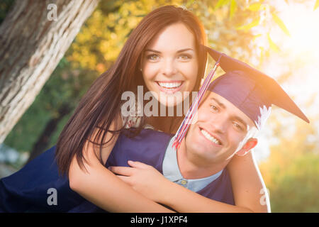 Heureux homme diplômé en Cap and Gown et jolie fille célébrer à l'extérieur. Banque D'Images