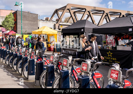 Street View de Brick Lane Market avec couple hipster et stands de nourriture à côté d'un des cycles de Santander station d'accueil. Brick Lane, Shoreditch, London, UK Banque D'Images