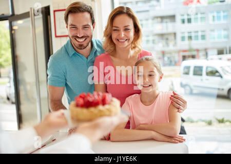 Famille satisfaits avec fille look de strawberry cake in bakery Banque D'Images