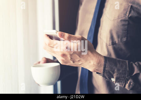 Close up business man holding smartphone et café dans le bureau avec la lumière du soleil. Filtre couleur vintage. Banque D'Images