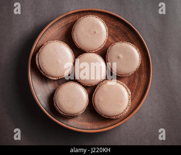 Macarons au chocolat brun pastel ou macarons sur une plaque sur fond sombre Banque D'Images