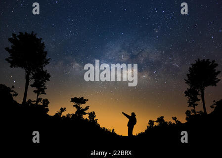 Un homme est debout à côté de la voie lactée pointant sur une étoile brillante dans la forêt, une longue exposition photo, avec du grain. Banque D'Images