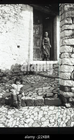 Fille ASSISE SUR UNE ÉTAPE ; FEMME DEBOUT PRÈS D'UNE PORTE. Banque D'Images